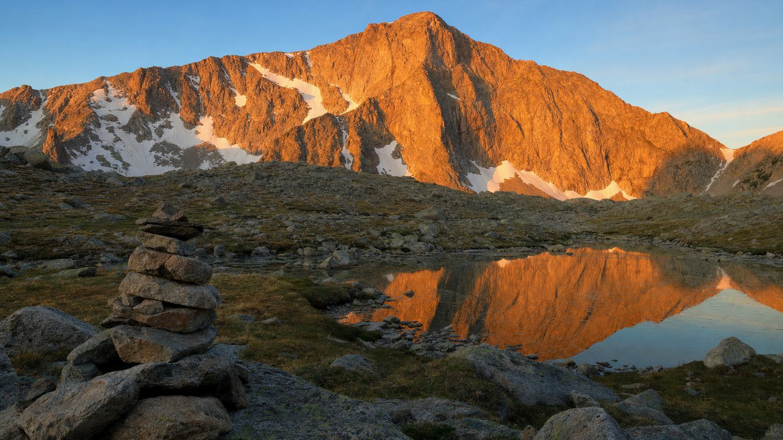 Lumière de l'aube sur un massif de granite et un petit lac de montagne, avec un cairn au premier plan