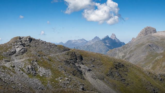 Randonneurs sur un sentier d'altitude face à une crête des Pyrénées, par temps clair en fin de matinée