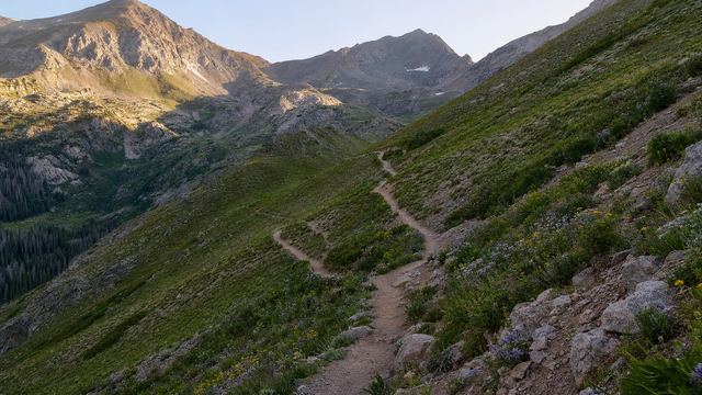 Senderistas caminando junto a un lago de alta montaña rodeado de cumbres y neveros en los Pirineos franceses