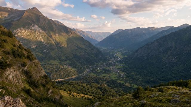 Vue d'ensemble d'une vallée pyrénéenne aux versants boisés, dominée par un grand sommet rocheux encore enneigé