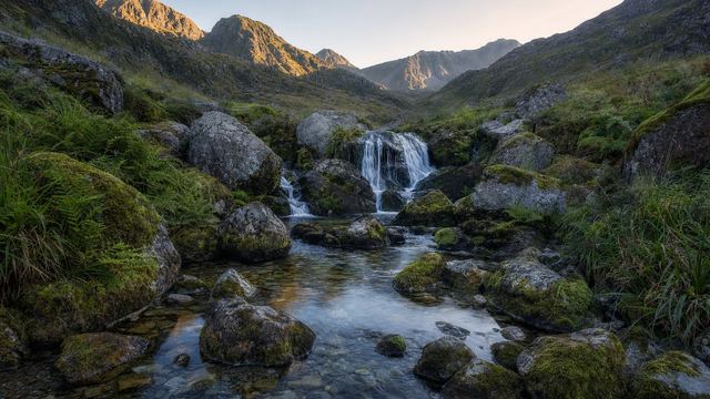 Pêcheur à la mouche au bord d'un lac d'altitude entouré de rochers et de pelouses, au petit matin